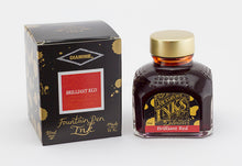 Load image into Gallery viewer, A glass bottle of 80ml Diamine Brilliant Red fountain pen ink next to its packaging box, in front of a white background.

