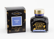 Load image into Gallery viewer, A glass bottle of 80ml Diamine Washable Blue fountain pen ink next to its packaging box, in front of a white background.
