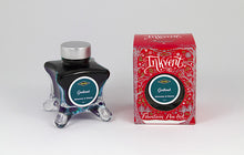 Load image into Gallery viewer, A glass bottle of 50ml Diamine Red Edition Inkvent Garland Shimmer &amp; Sheen fountain pen ink next to packaging box, in front of a white background.
