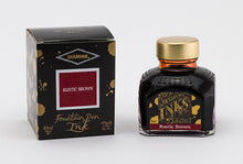 Load image into Gallery viewer, A glass bottle of 80ml Diamine Rustic Brown fountain pen ink next to its packaging box, in front of a white background.
