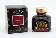 Load image into Gallery viewer, A glass bottle of 80ml Diamine Oxblood fountain pen ink next to its packaging box, in front of a white background.
